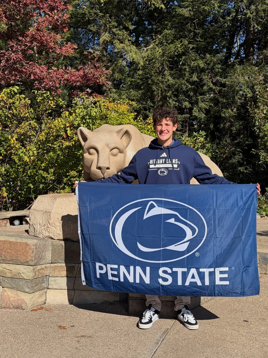 Connor Minear holding a Penn State flag beside the campus lion statue