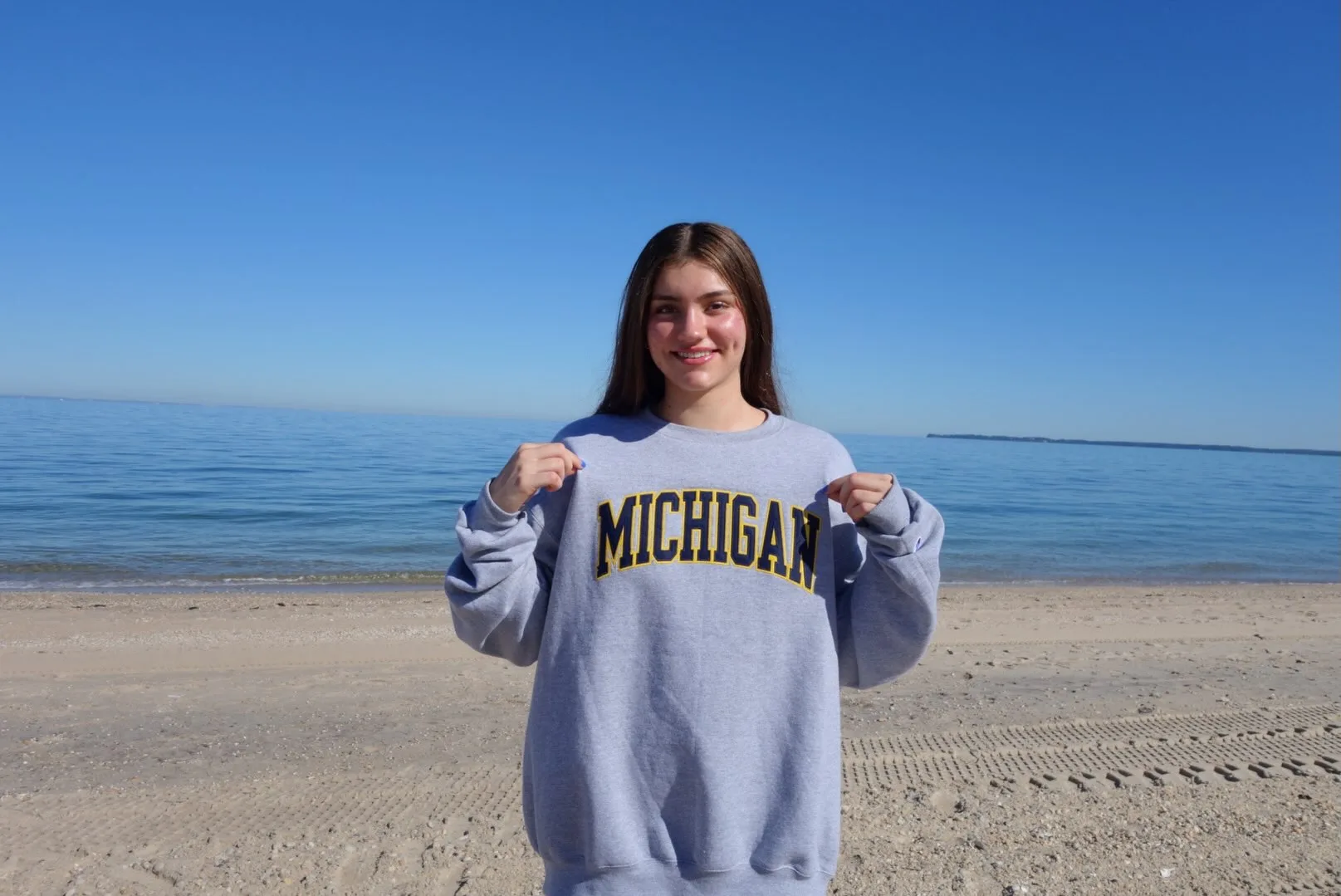 Julia Lucca holding her Michigan sweatshirt beside the water